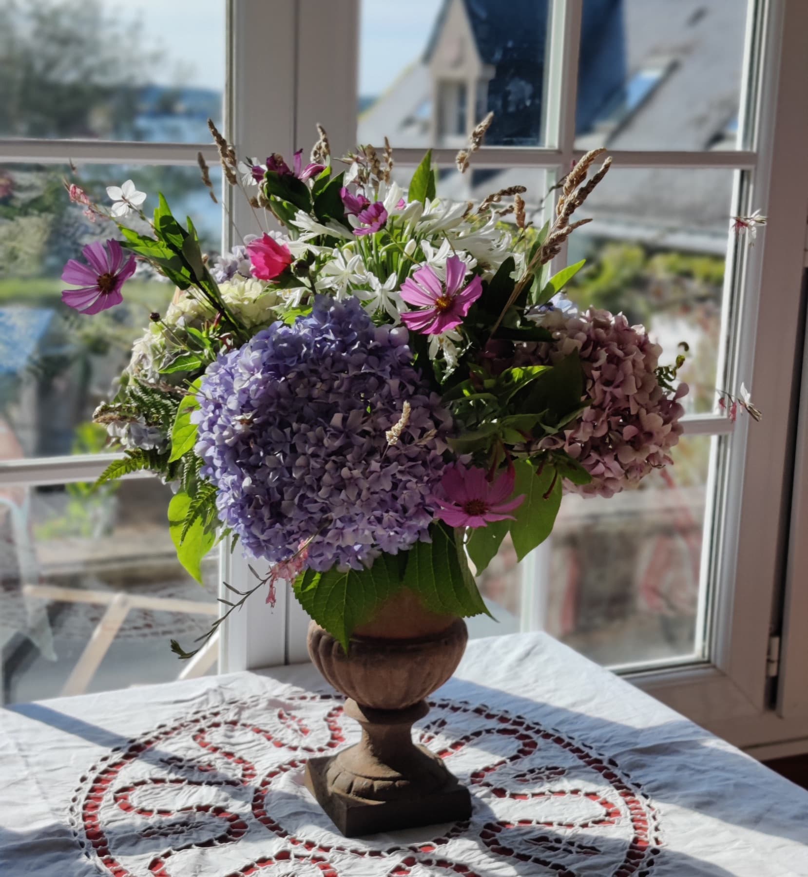 Coupe d’hortensias bleus et roses posée devant une fenêtre à petits carreaux